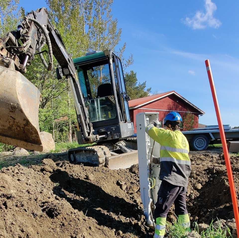 Kaivinkone ja asentaja asentamassa kaapelointikaappia kaivantoon